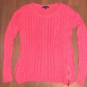Coral sweater with zipper accents on sides.